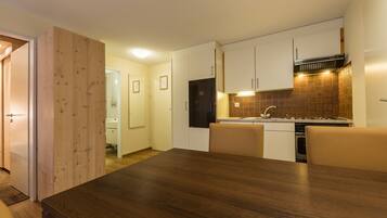 Une cuisine moderne avec des meubles en bois, un four encastré et un coin repas comprenant une table et des chaises en bois.