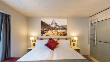 A hotel room with a bed, two bedside lamps, a red pillow, a painting of a mountain, and a ladder against the wall.