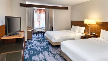 A hotel room with two beds, a TV, a desk, a chair, and a lamp.