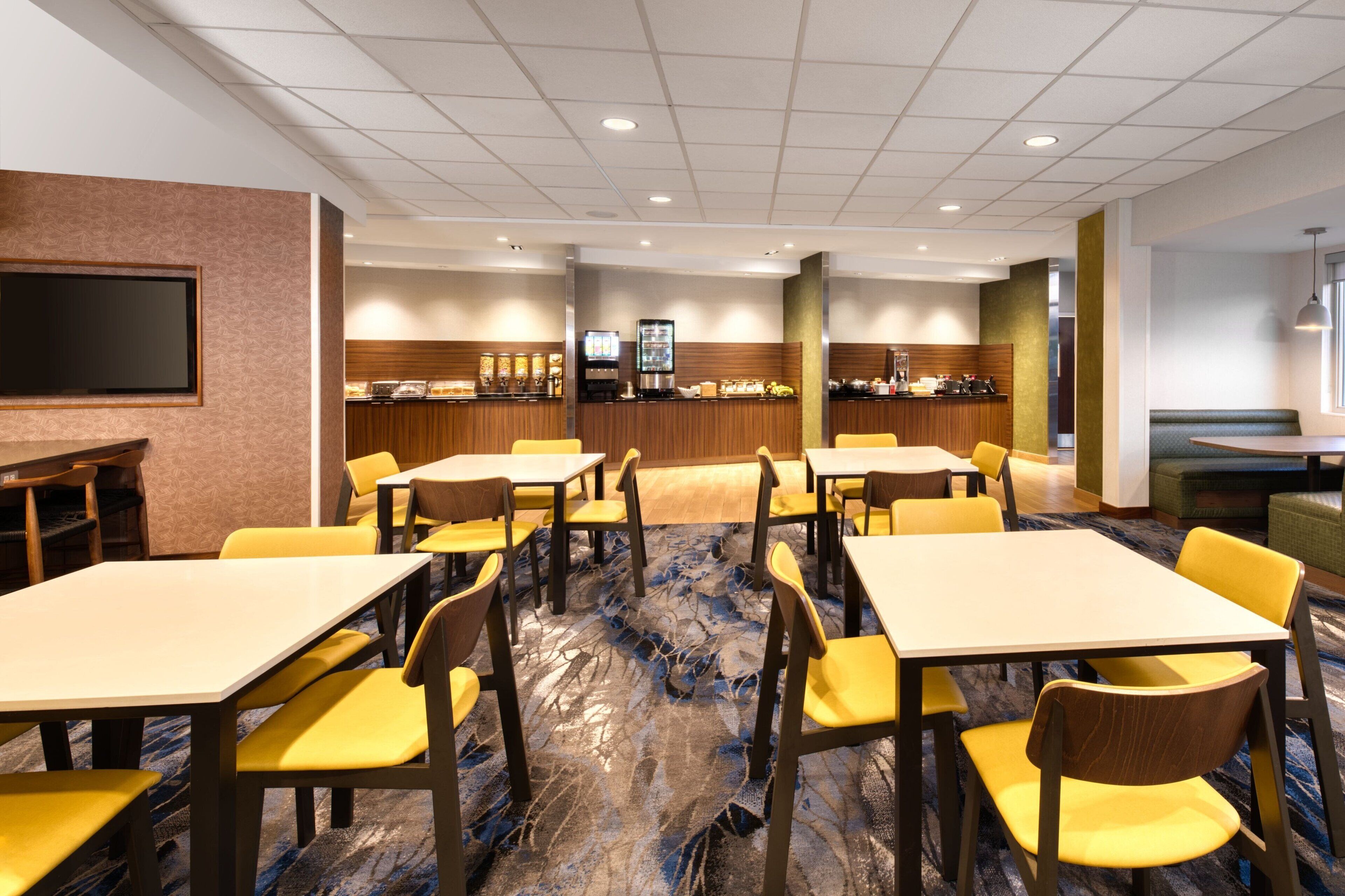 A hotel lobby with multiple tables and chairs, a reception area, and a large screen.