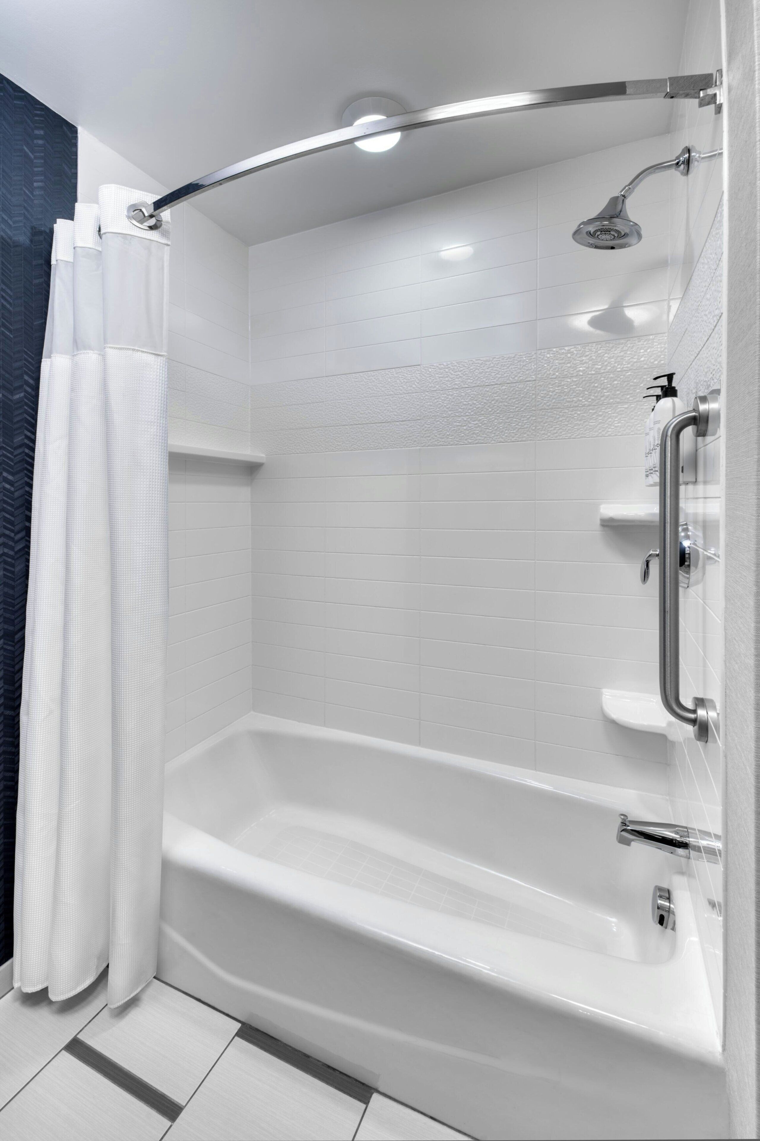 Una ducha moderna con puerta de vidrio curva, cabezal de ducha manual y barra de soporte para ducha.