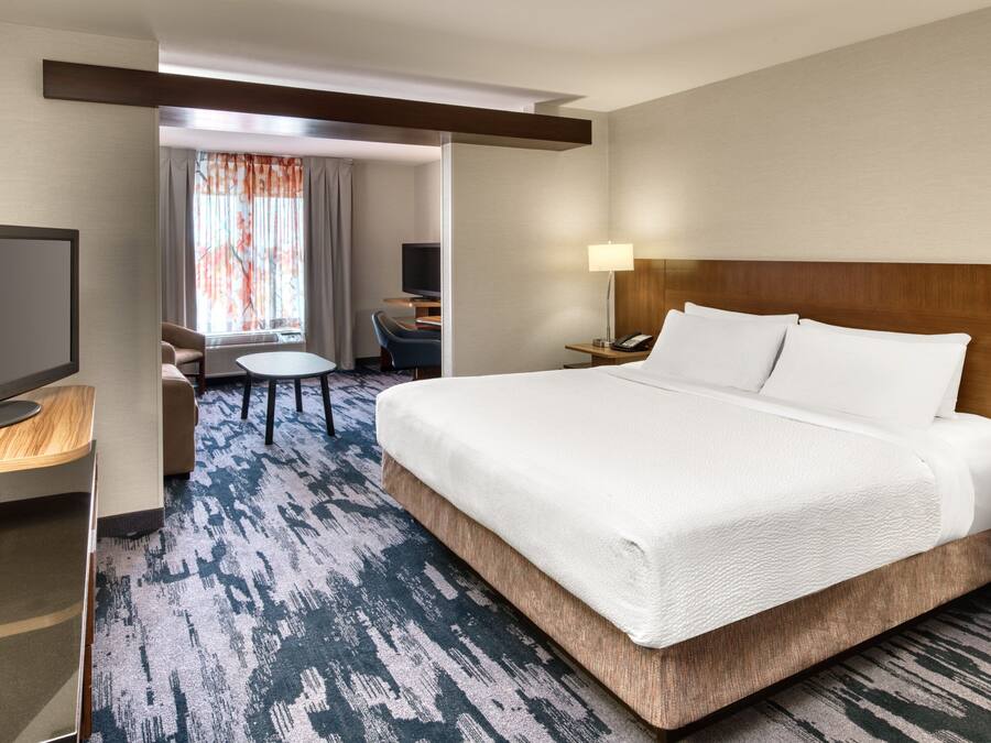 Una habitación de hotel con una cama grande, un escritorio con televisor de pantalla plana, una silla y una mesita.