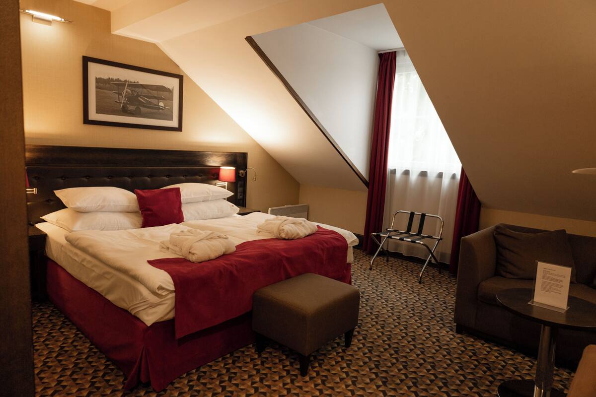 A hotel room with a bed, a chair, a small table, and a framed picture on the wall.