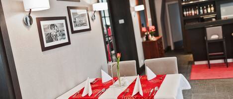 A restaurant with tables set for dining, framed pictures on the wall, and a bar area in the background.
