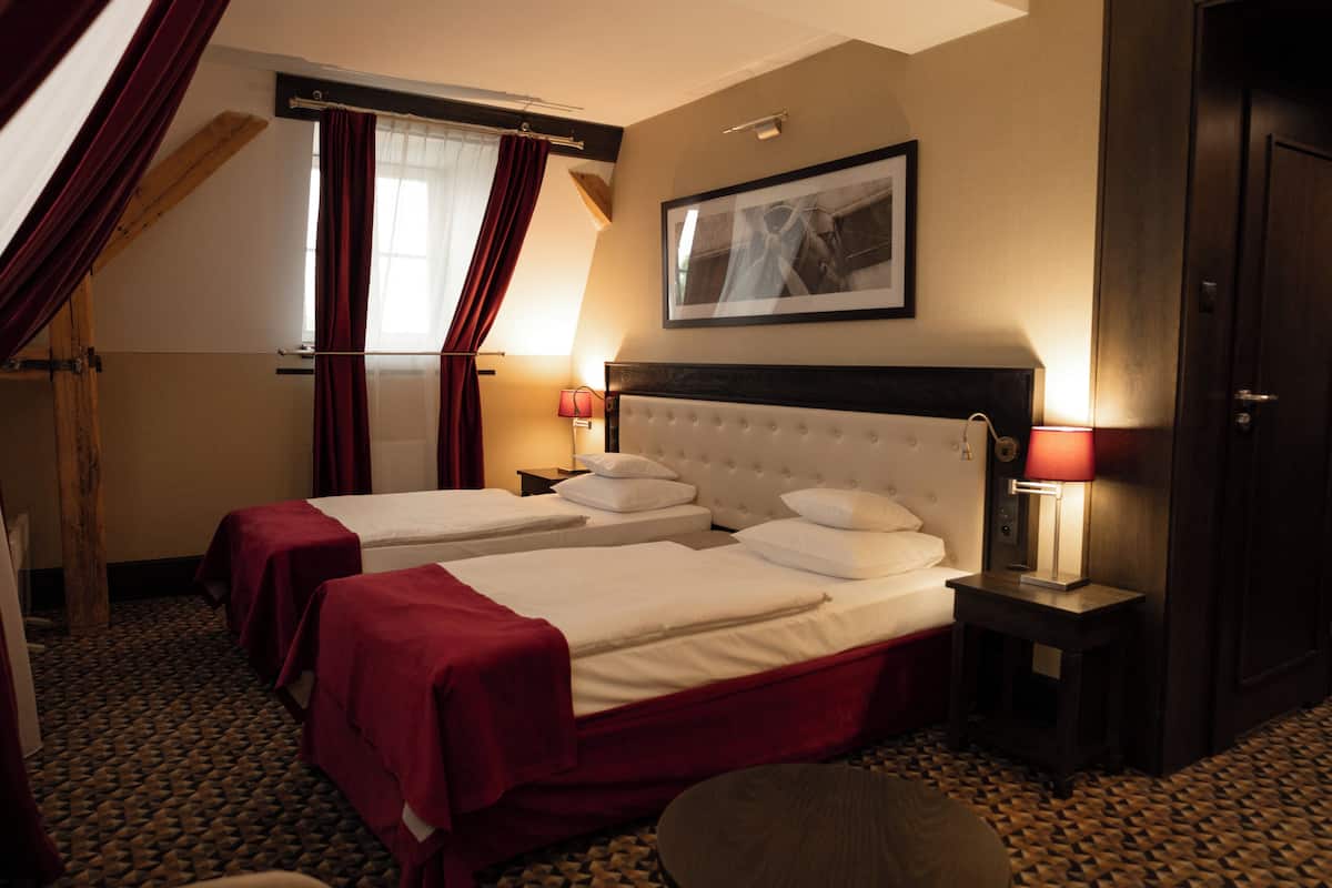 A hotel room with two beds, a large framed picture on the wall, and a window with curtains.