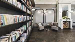 A library with bookshelves, two armchairs, a fireplace, and a small table. - Hotel Red Baron (Swidnica)