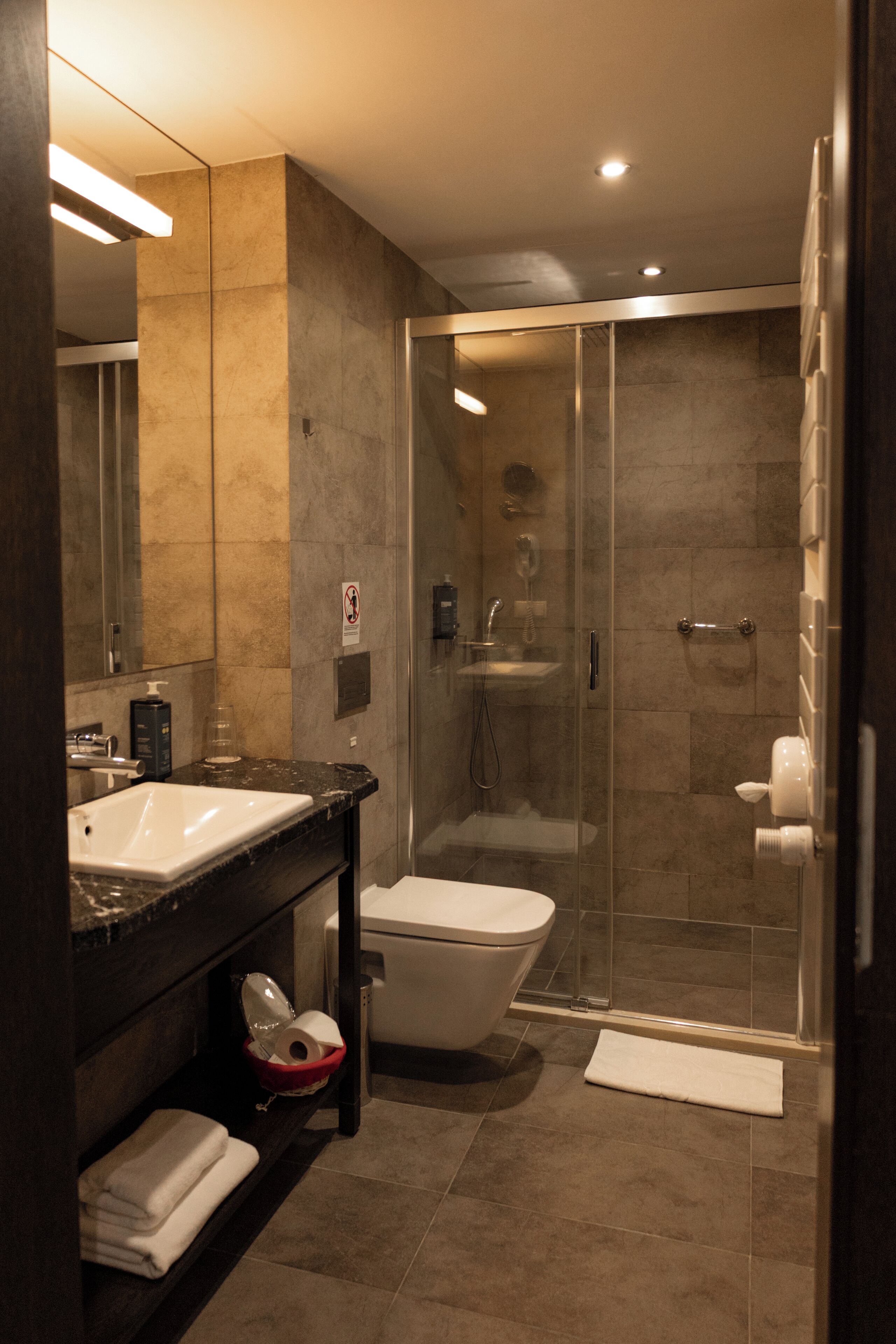 A modern bathroom with a glass-enclosed shower, a white toilet, and a dark marble sink.
