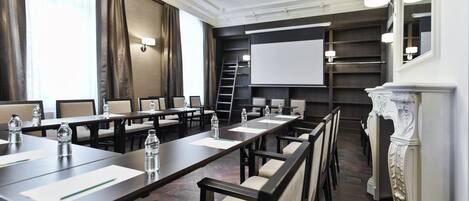 A conference room with a long table, chairs, a projector screen, and a fireplace.