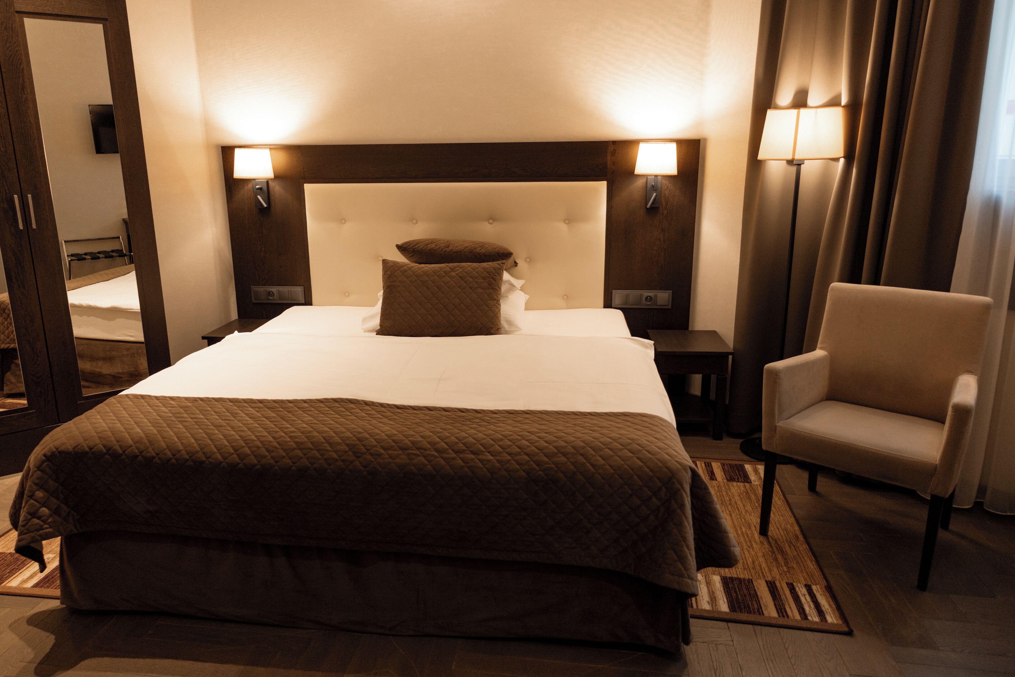 A hotel room with a large bed, two bedside lamps, a chair, and a mirror.