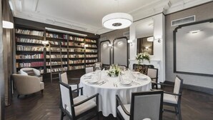 A library-style dining area with a round table set for six, surrounded by bookshelves filled with books. - Hotel Red Baron (Swidnica)