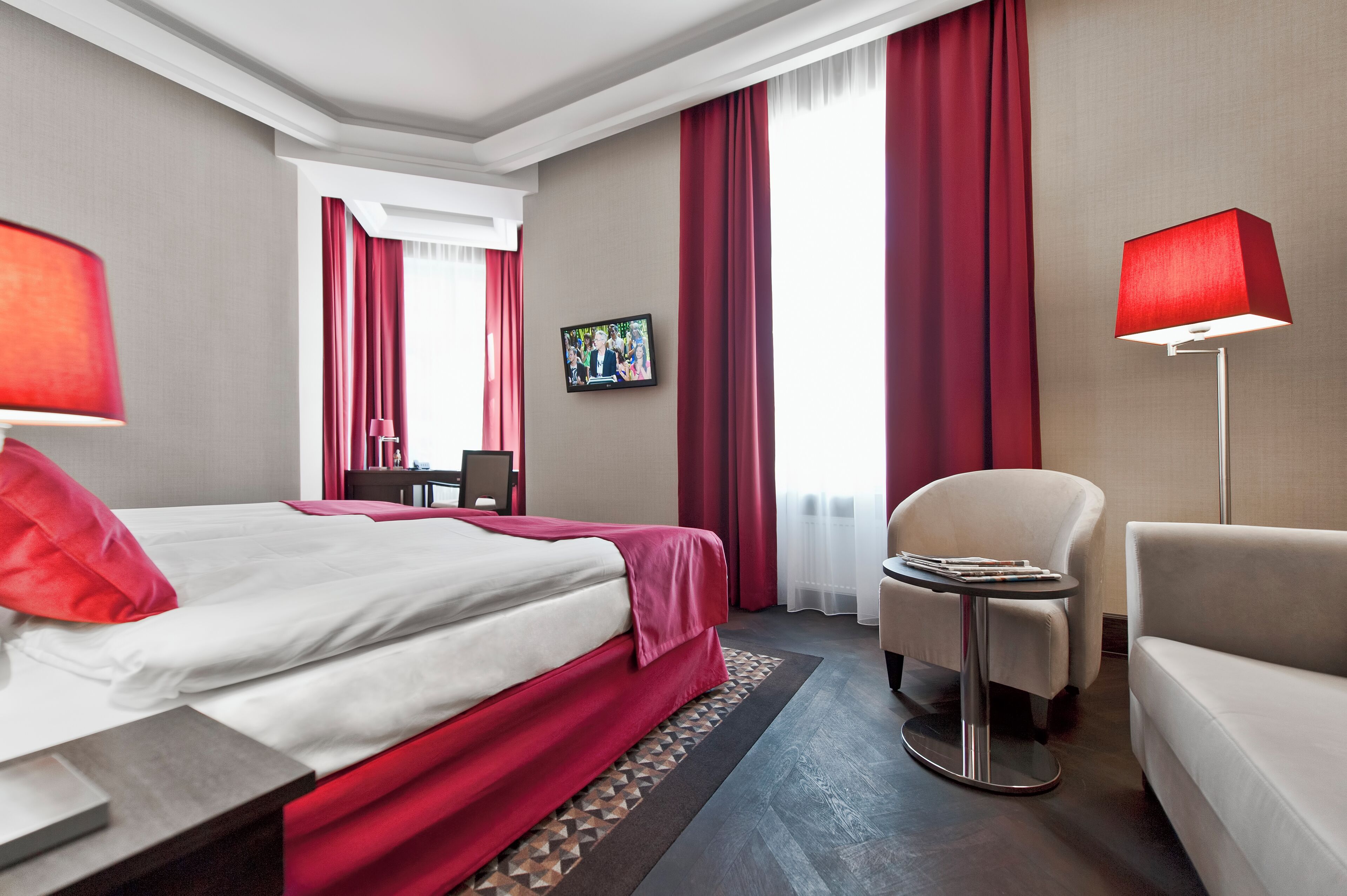 Une chambre d’hôtel avec un lit, un bureau, une chaise, un canapé et un téléviseur fixé au mur.