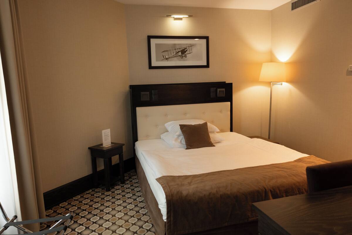 A hotel room with a bed, bedside table, lamp, and a framed picture on the wall.