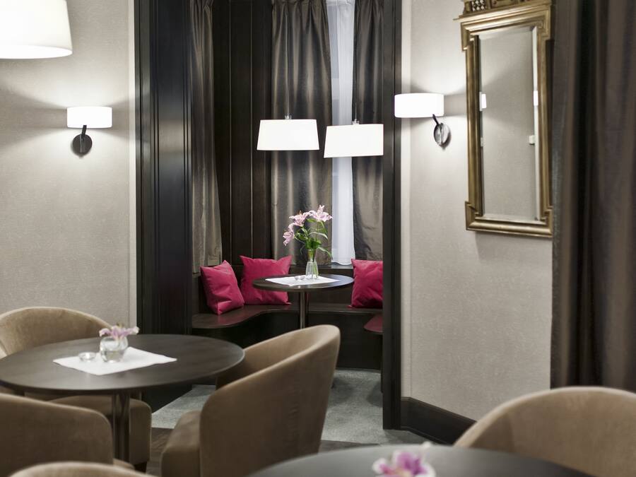 Ein Hotelzimmer mit Essbereich, ausgestattet mit runden Tischen, beigen Stühlen und einem kleinen Tisch mit Blumen in einer Vase.