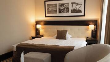 Habitación de hotel con una cama grande, dos lámparas de noche, un cuadro enmarcado sobre la cama, una pequeña mesa redonda con una silla y un suelo estampado.