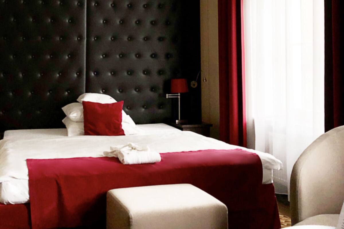A hotel room with a large bed, a red accent wall, and a window with curtains.