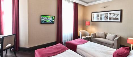 Habitación de hotel con dos camas, un escritorio, una silla, un televisor y un cuadro en la pared.