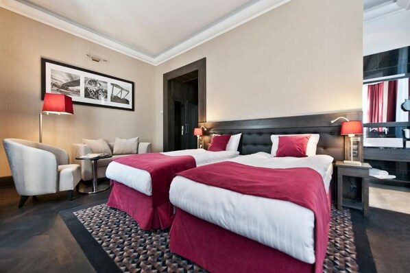 Habitación de hotel con dos camas, un sofá, una silla, una mesita y un cuadro en la pared.