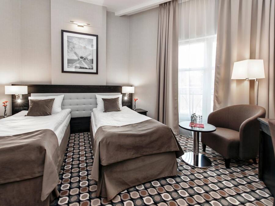 Hotellihuone, jossa on kaksi sänkyä, sohva, pieni pöytä ja lamppu.