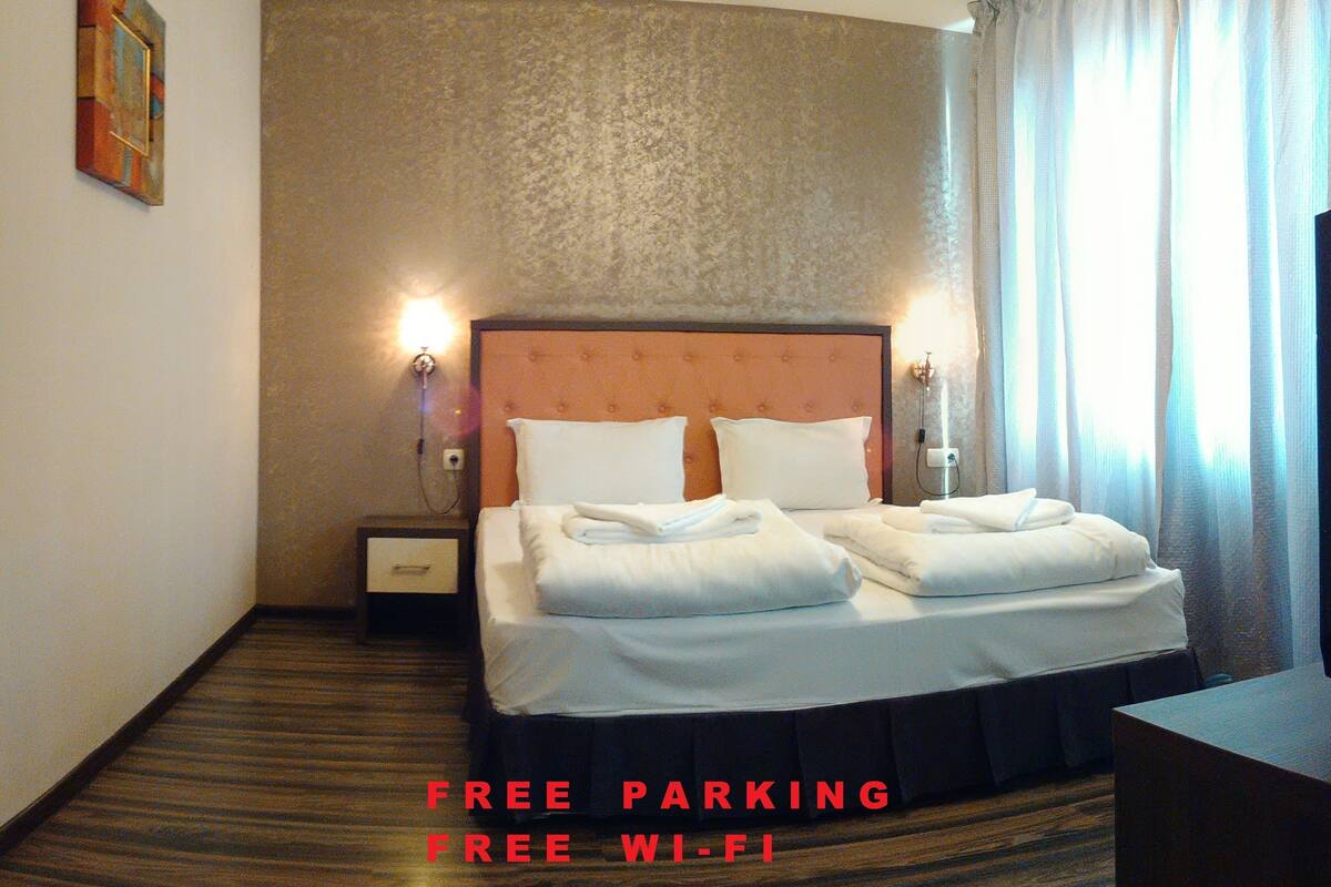A hotel room with a bed, nightstands, and a view of the outdoors.