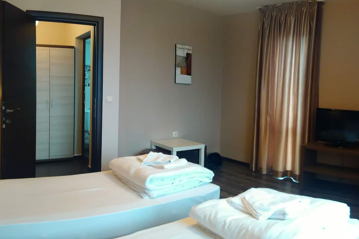 A hotel room with two beds, a small table, a TV, and a door leading to another room.