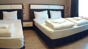 A hotel room with two beds, each with white linens and pillows, a nightstand with a lamp, and a window with curtains. - City Hotel Blagoevgrad (Blagoevgrad)