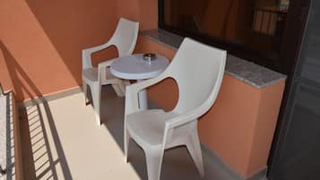 A small outdoor seating area with two white plastic chairs and a round table, adjacent to a building with a glass door and a window.