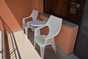 A small outdoor seating area with two white plastic chairs and a round table, adjacent to a building with a glass door and a window. - City Hotel Blagoevgrad (Blagoevgrad)