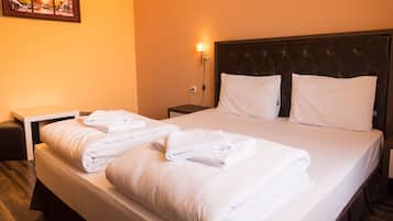 A neatly made bed with white linens and pillows, a bedside table with a lamp, and a wall-mounted picture.
