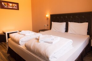 A neatly made bed with white linens and pillows, a bedside table with a lamp, and a wall-mounted picture. - City Hotel Blagoevgrad (Blagoevgrad)