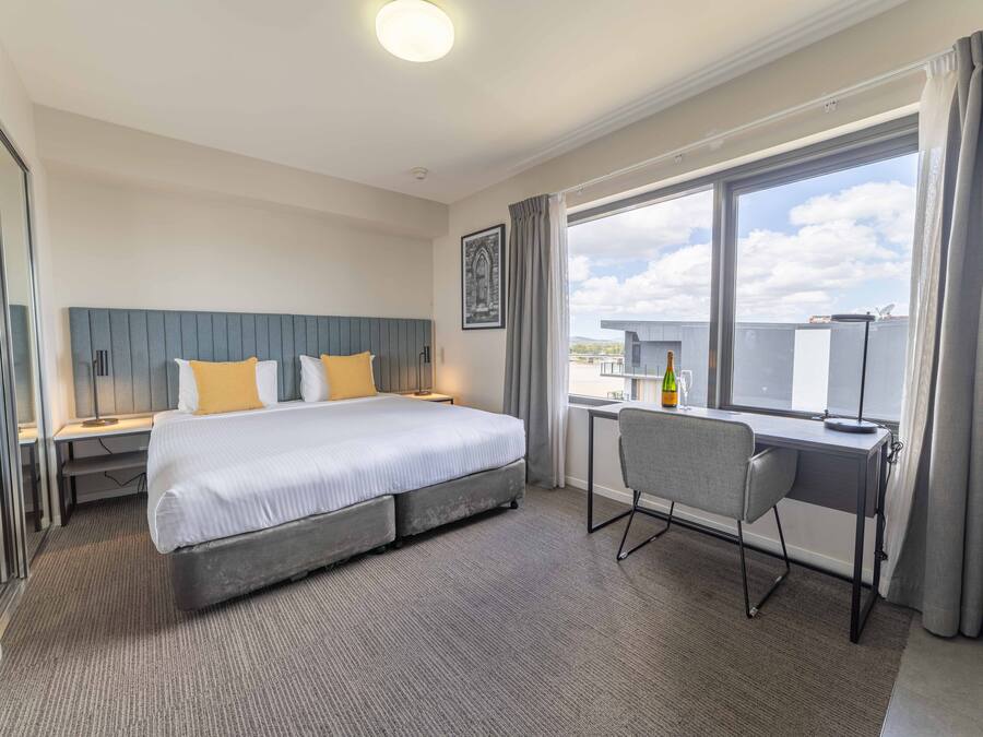 A hotel room with a large bed, a desk, and a window with curtains.