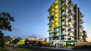 A multi-story hotel with balconies, a well-lit entrance, and a view of the surrounding area.