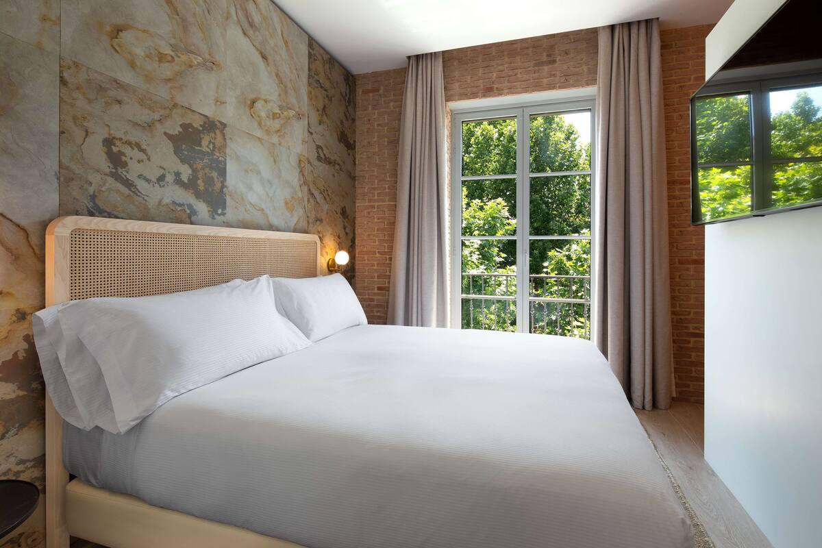 Een moderne hotelkamer met een groot bed, een bakstenen muur en een raam met gordijnen.