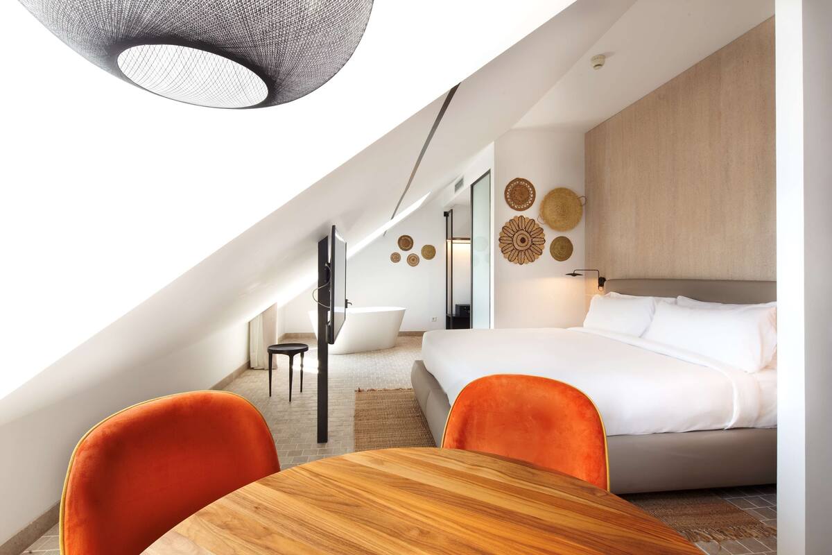 Een moderne slaapkamer met een groot bed, een eettafel en oranje stoelen.