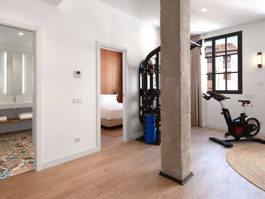 A hotel room with a bed, a bathroom with a mirror, a treadmill, and a large window.