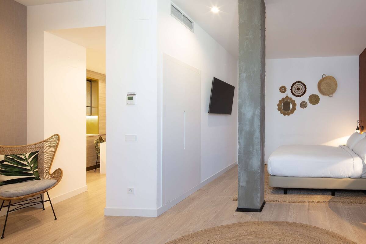Een moderne slaapkamer met een bed, een stoel, een aan de muur bevestigde televisie en decoratieve wandkunst.