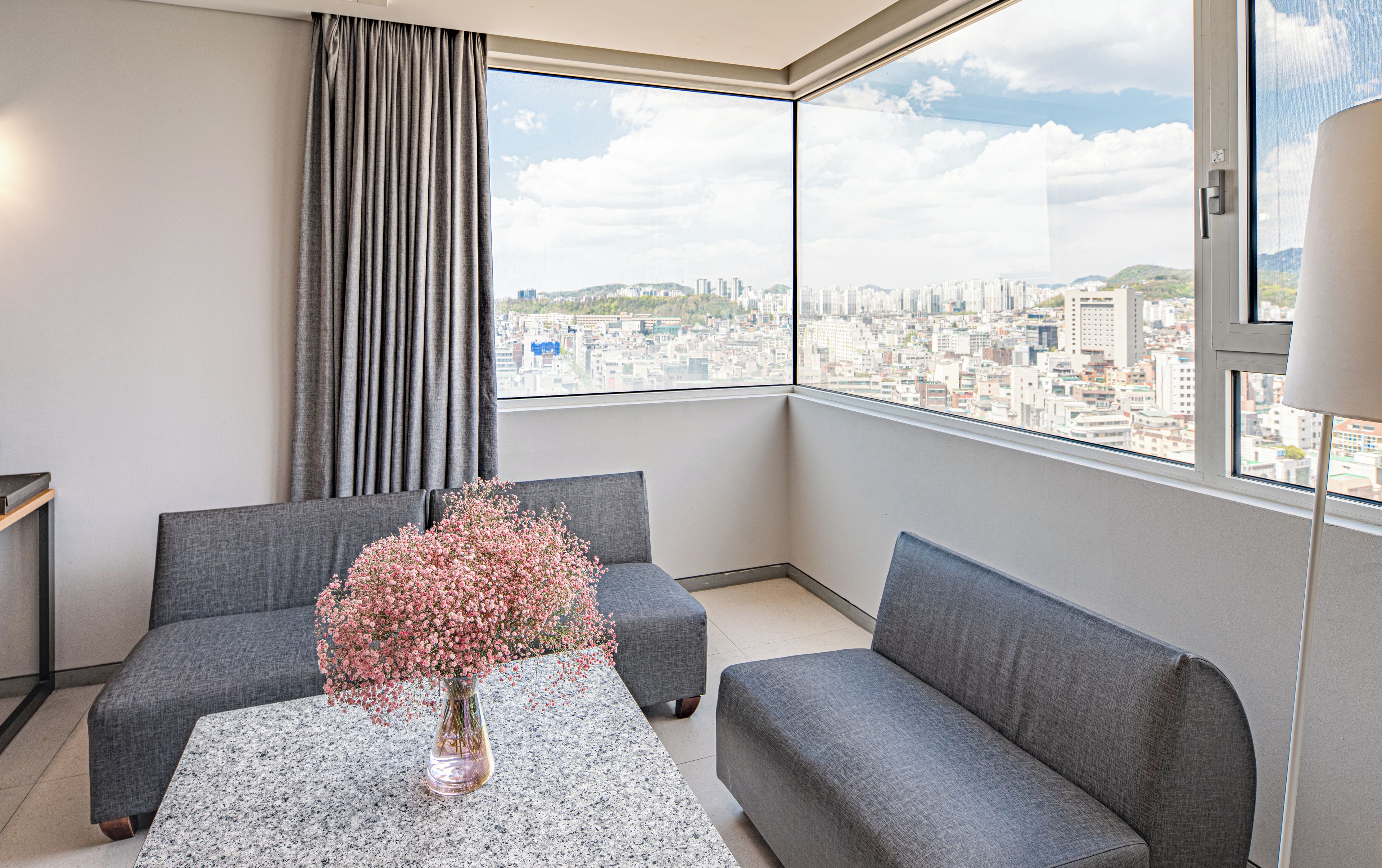 A modern living room with a city view, two grey sofas, a coffee table, and a vase with flowers.
