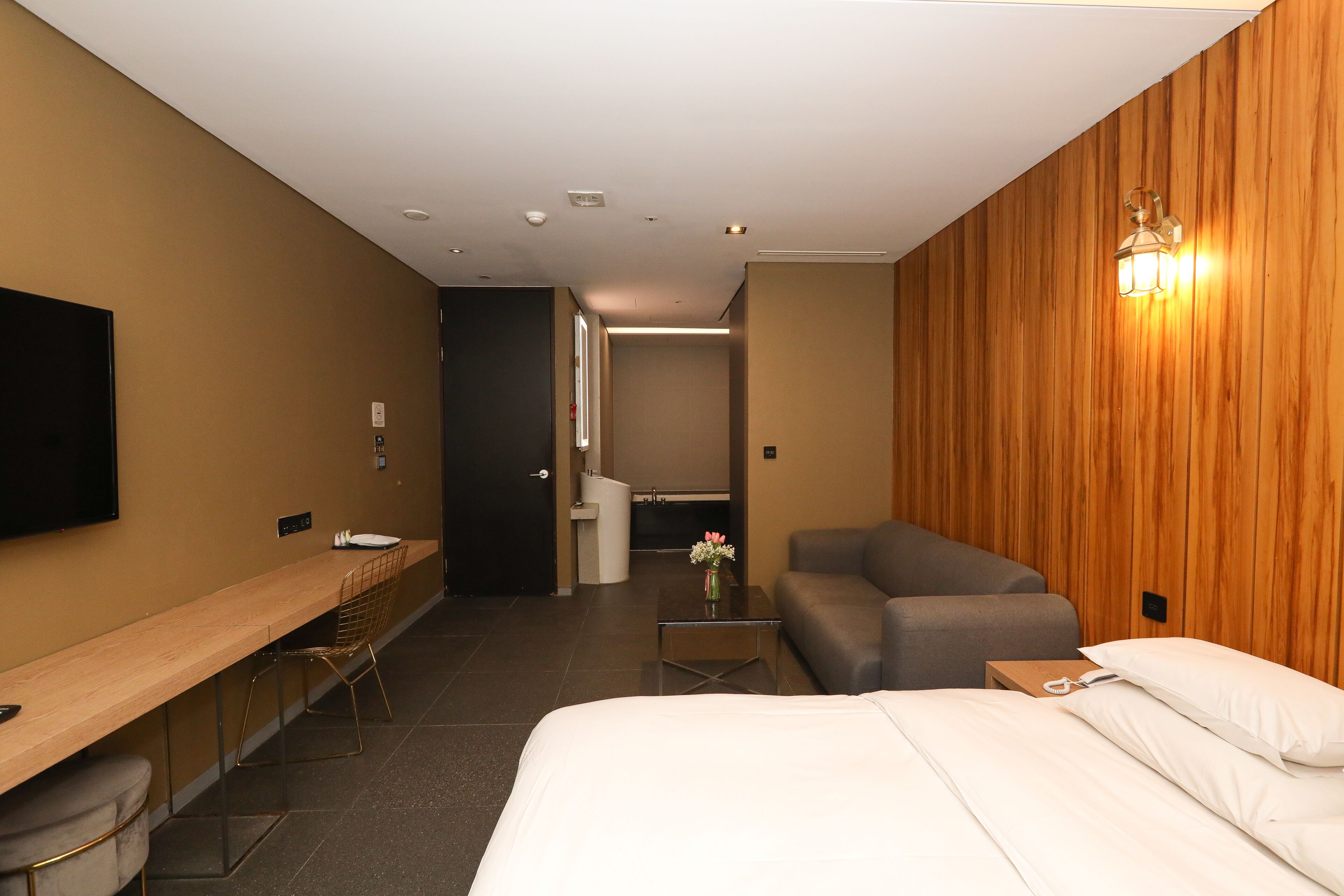 A modern hotel room with a bed, a sofa, a desk, and a TV.