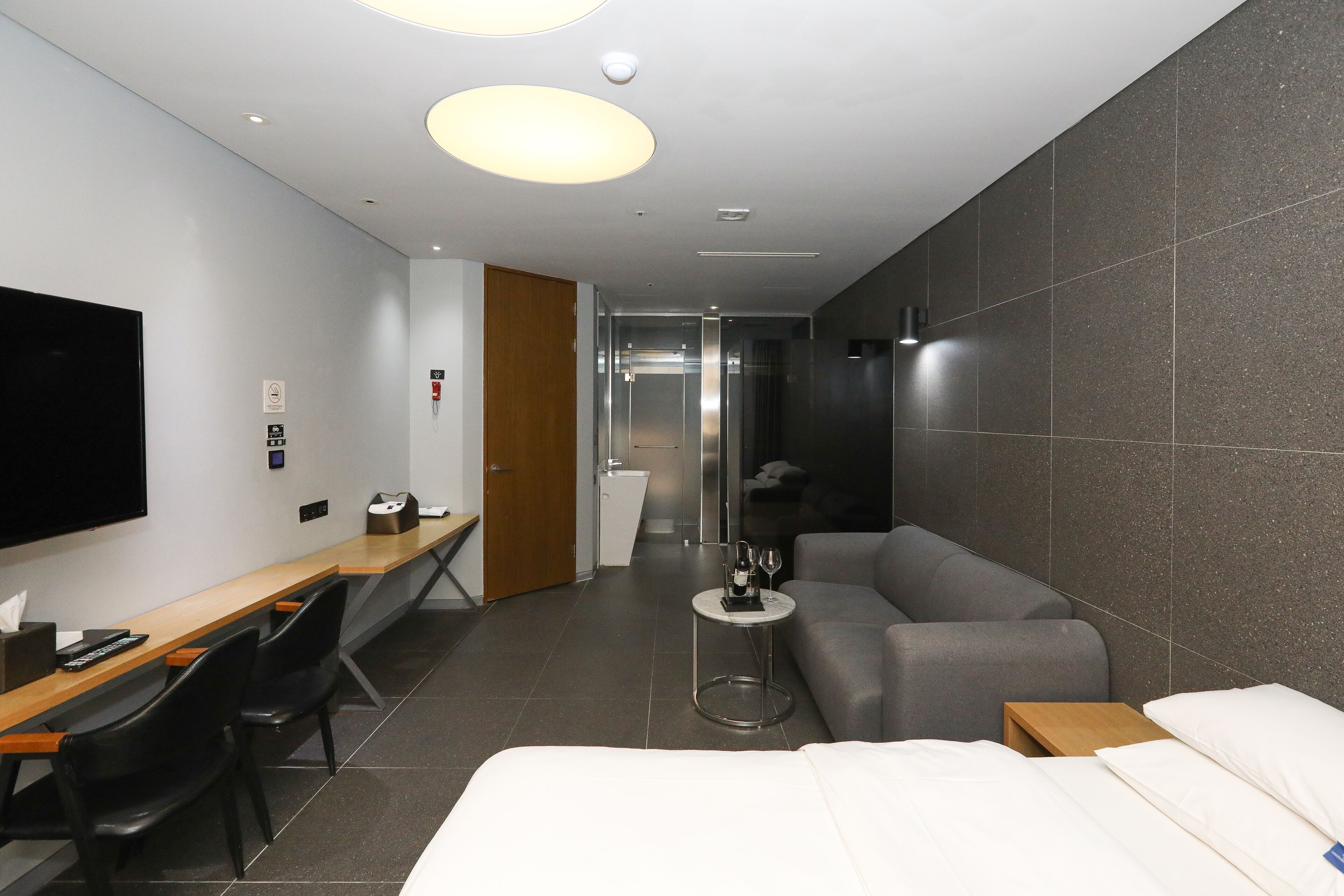 Et moderne hotelværelse med seng, sofa, skrivebord med stole, fjernsyn og et lille bord med et glas.