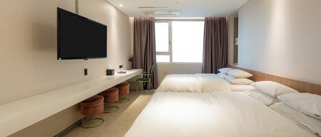 A hotel room with a flat-screen TV mounted on the wall, a large window with curtains, two beds with white linens, a long counter with stools, and a trash bin.
