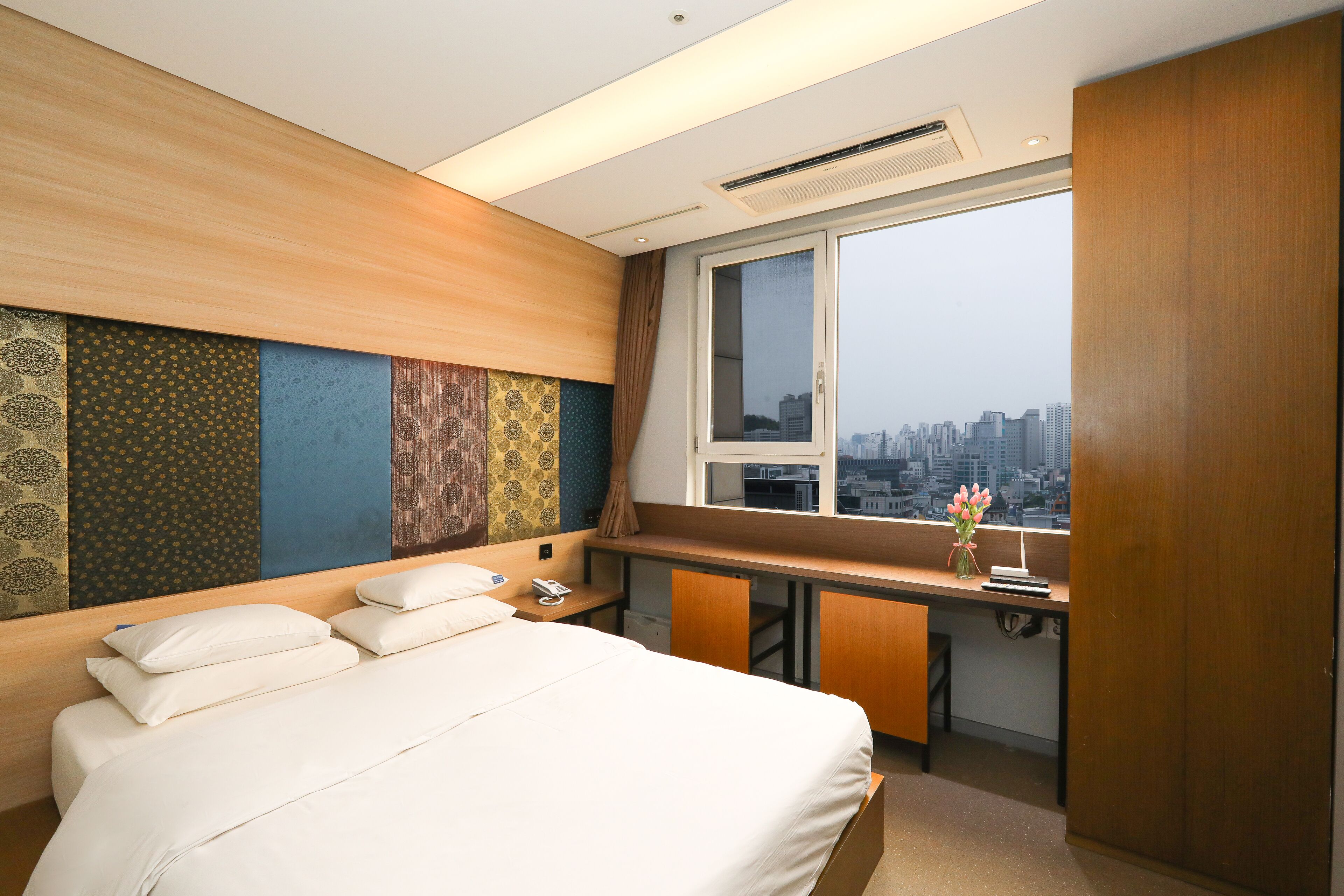 A hotel room with a bed, desk, and window with a city view.