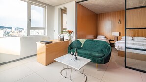 A modern room with a city view, a green velvet sofa, a small table with a bottle and glass, and a bed with white linens. - Hotel The Designers Hongdae (Seoul)