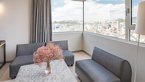 A modern living room with grey sofas, a coffee table, and a vase of flowers. A large window offers a city view. - Hotel The Designers Hongdae (Seoul)