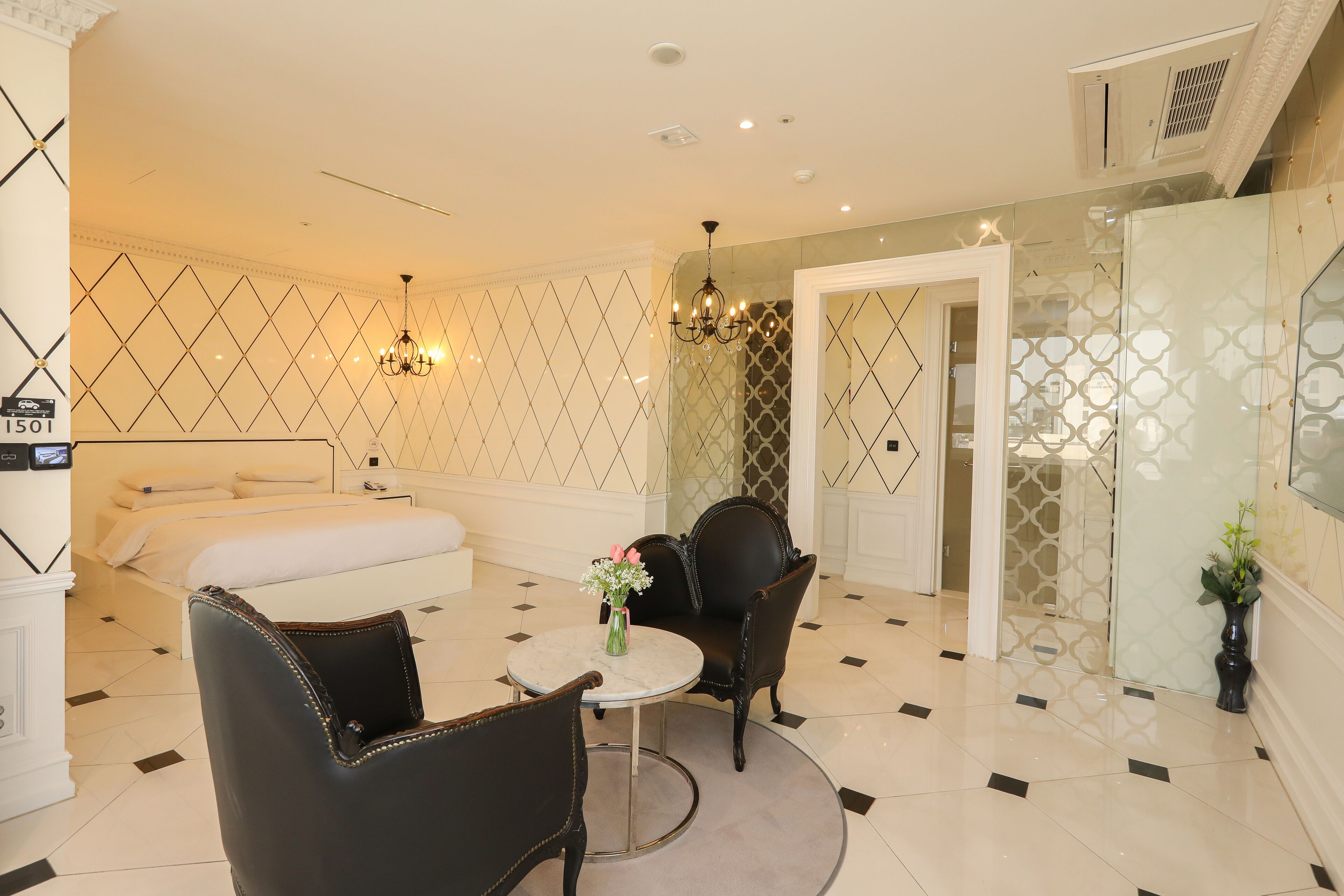 A hotel room with a bed, two chairs, a small table, and a vase of flowers.