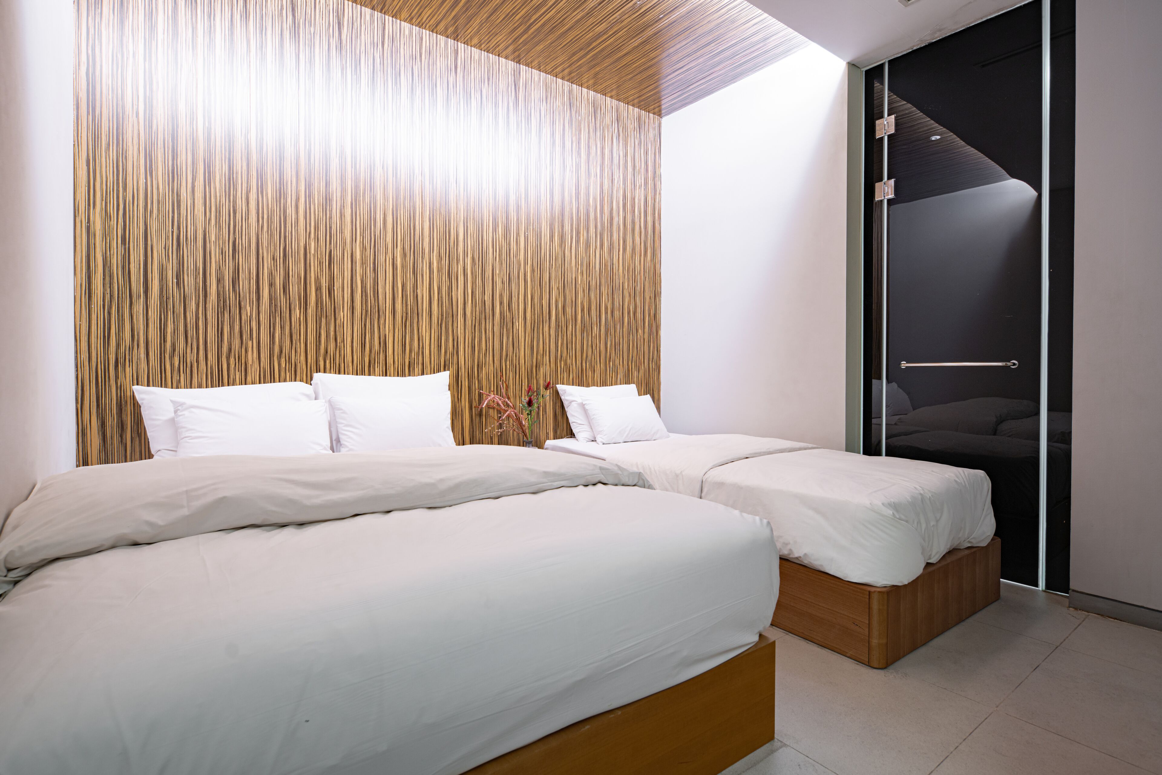 A modern bedroom with two beds, a wooden slatted headboard, and a sliding door closet.