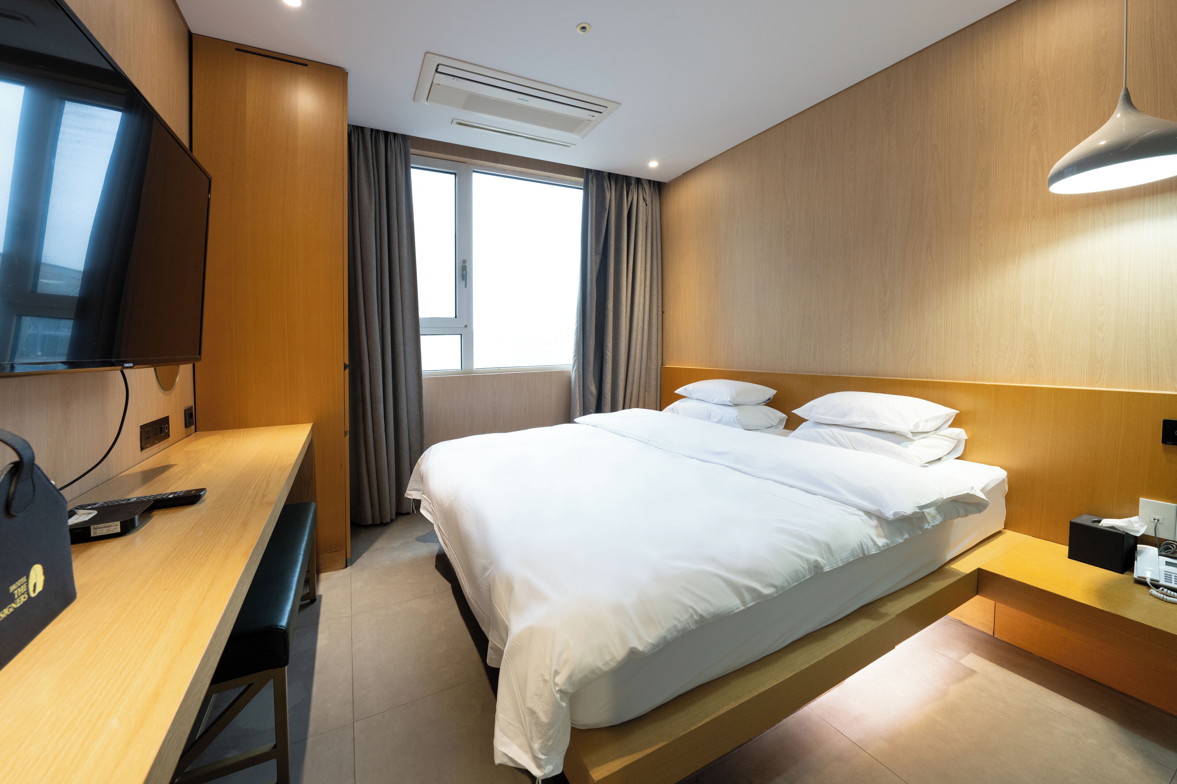 A modern hotel room with a large bed, a desk with a computer, a TV, and a window with curtains.