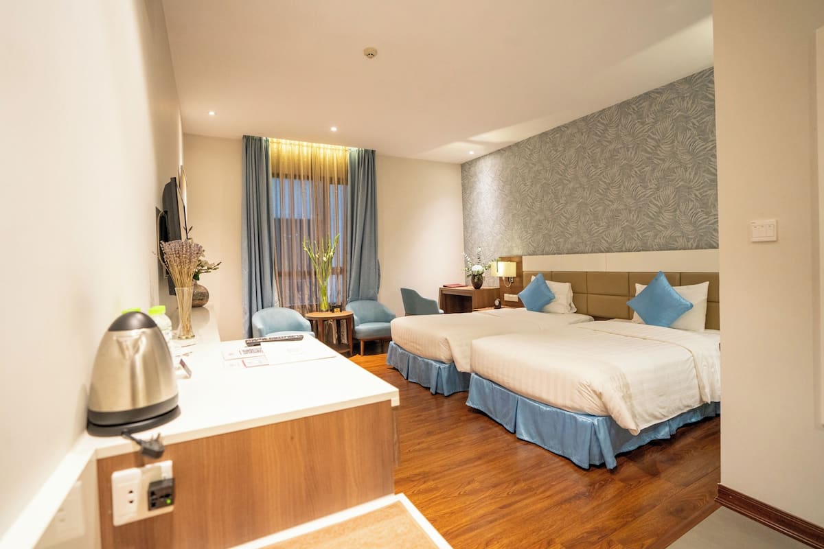 A hotel room with two beds, a desk, a chair, a nightstand, and a large window with curtains.
