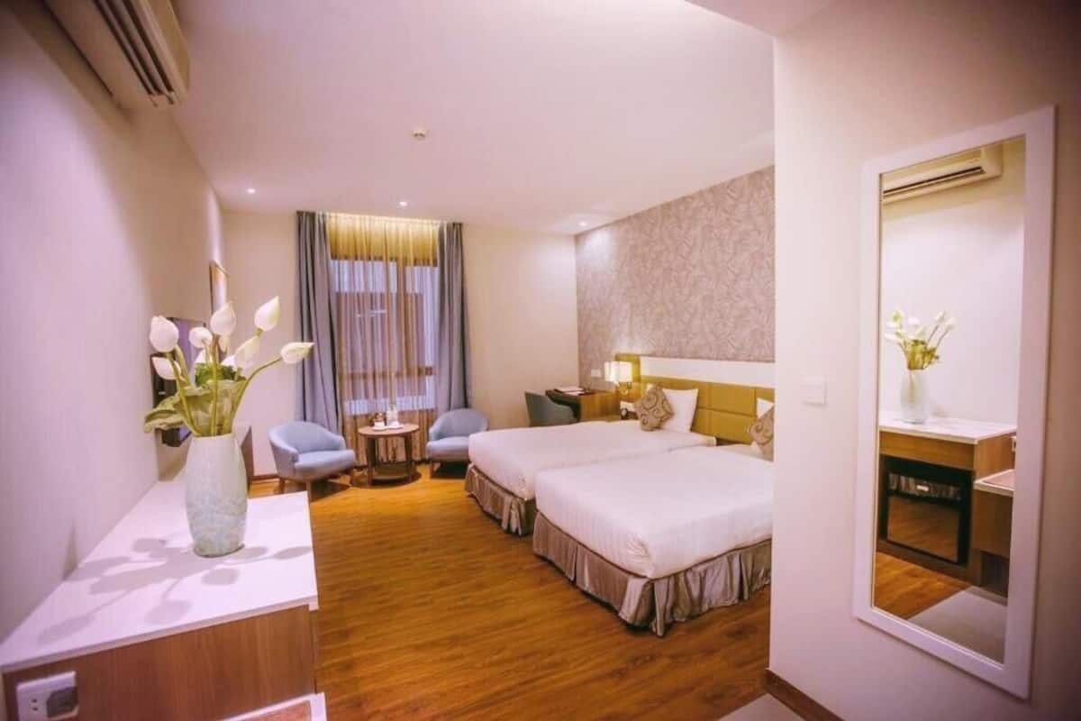 A hotel room with two beds, a desk, a chair, a small table, and a mirror.