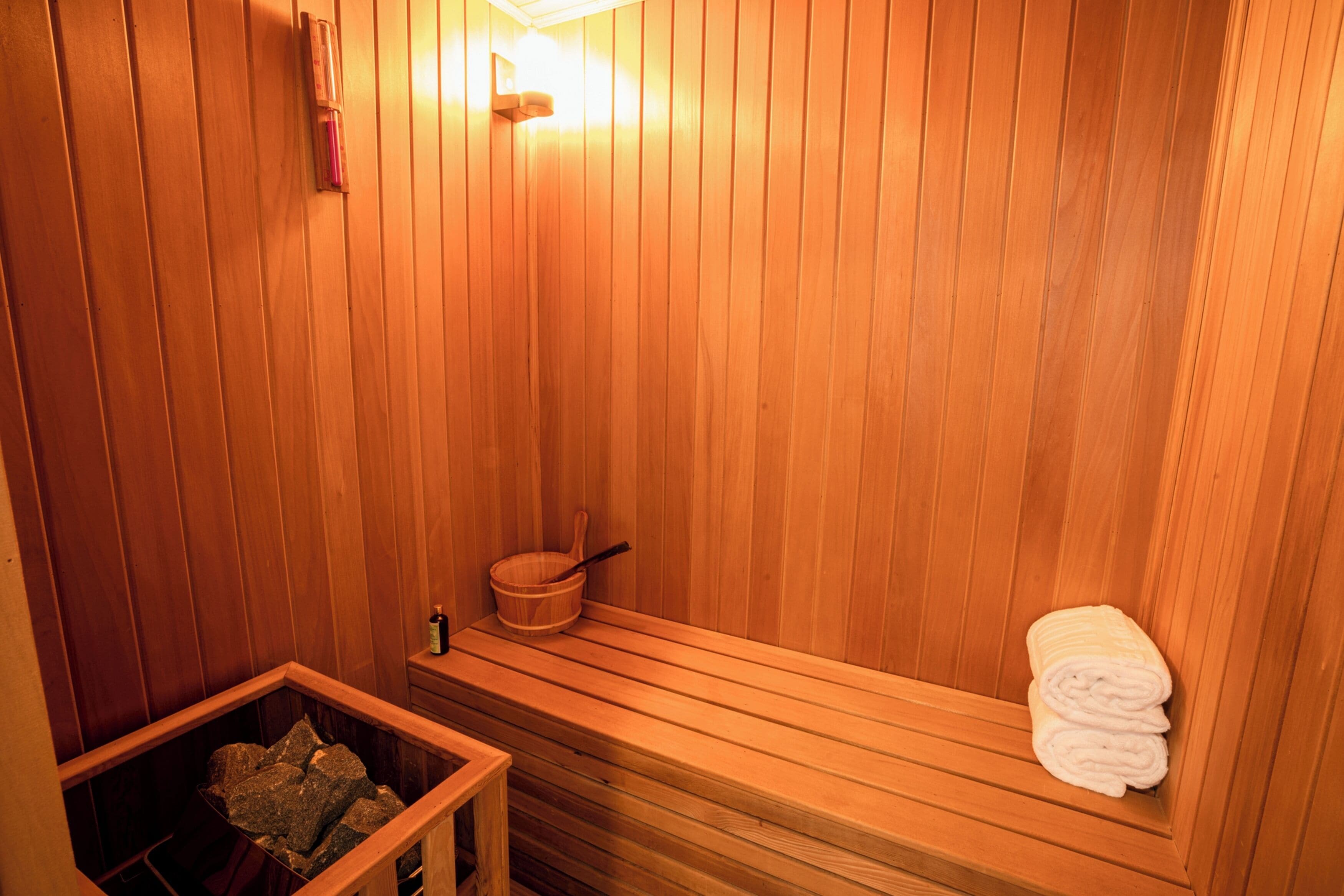 A wooden sauna with benches, a wooden bucket, and a towel rack.