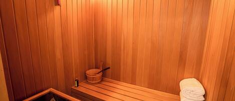 A wooden sauna with benches, a wooden bucket, and a towel rack.