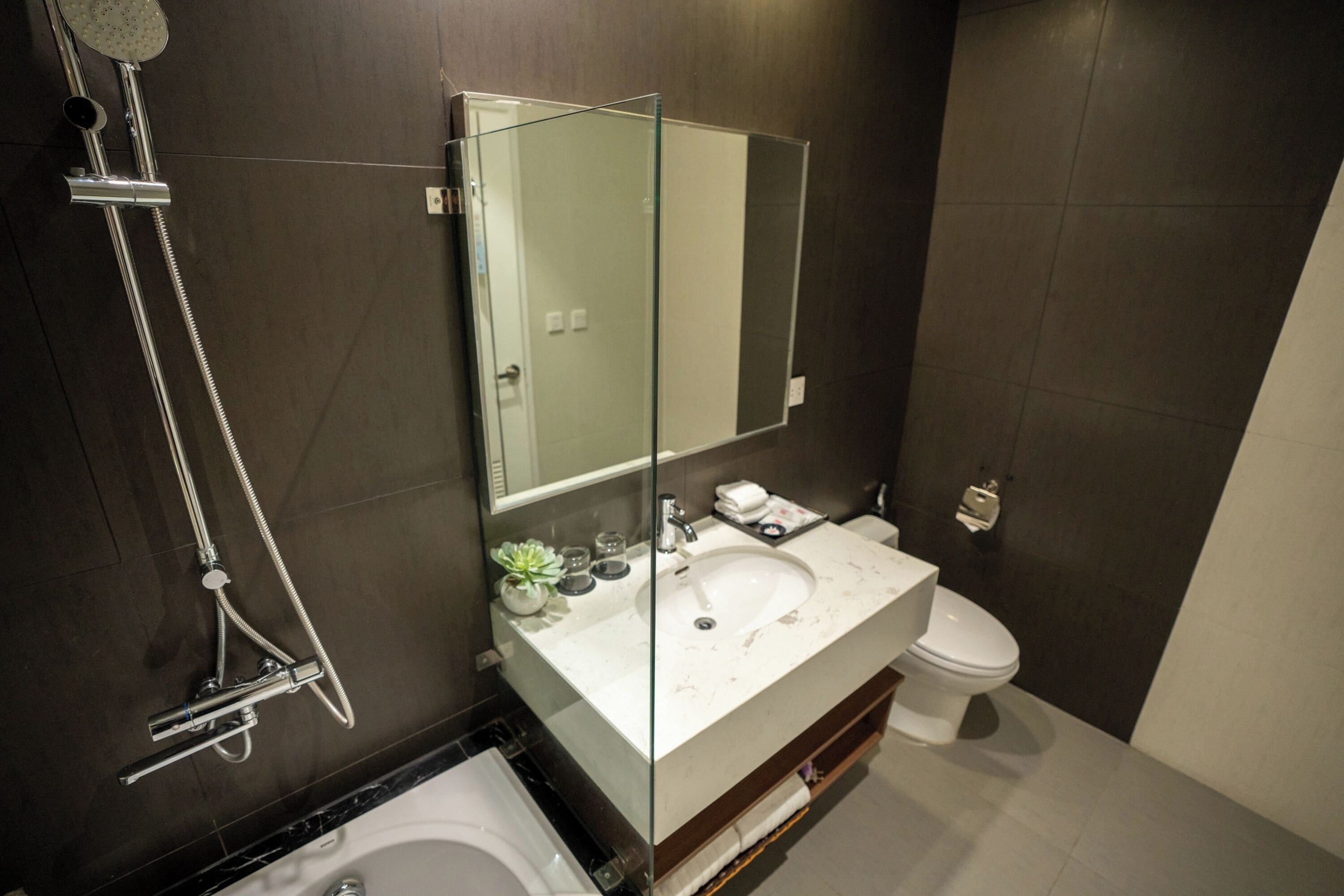 Un baño moderno con ducha envuelta en vidrio, un lavamanos blanco sobre encimera de mármol y un inodoro.